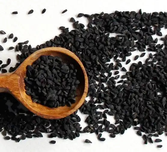 Black cumin seeds scattered around a wooden spoon.