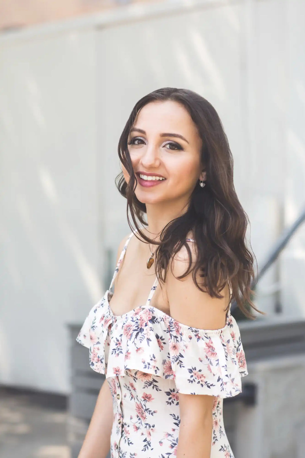 A smiling woman wearing a floral off-shoulder summer dress.